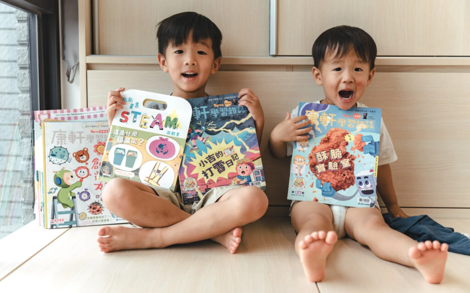 兩個孩子坐在窗邊,手拿康軒學習雜誌與 STEAM 遊戲書