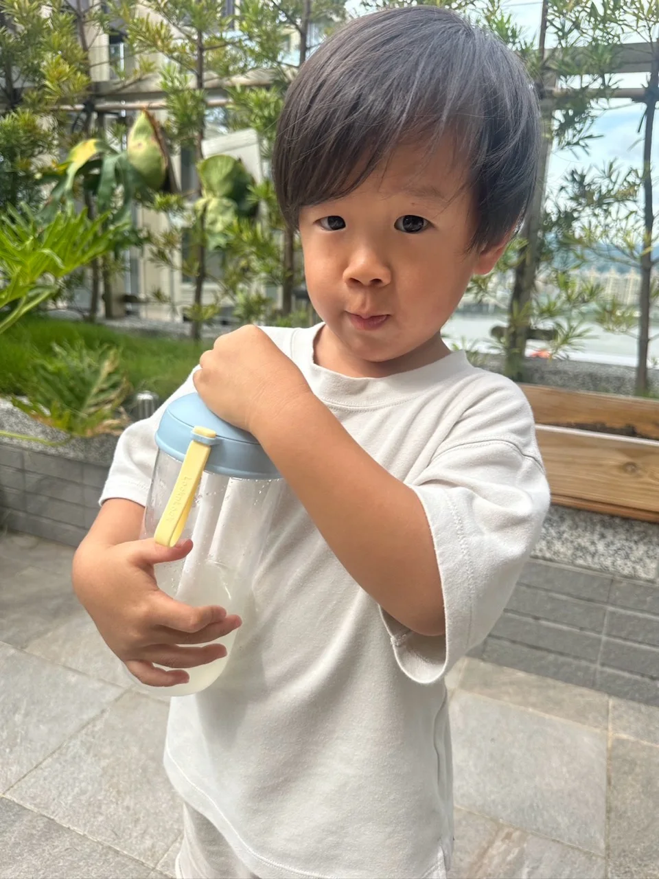 孩子在戶外雙手抱著藍色杯蓋的樂扣透明杯