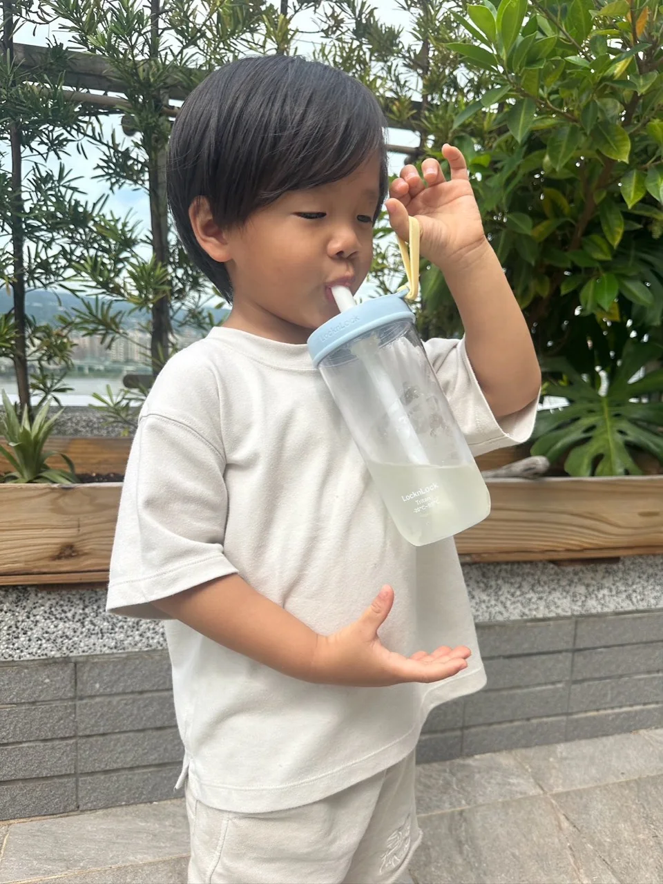 孩子用吸管喝水，一手提起杯蓋上的黃色提帶