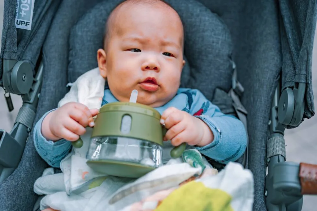 坐在推車上的孩子拿著 ALICE 嬰幼兒吸管杯喝水