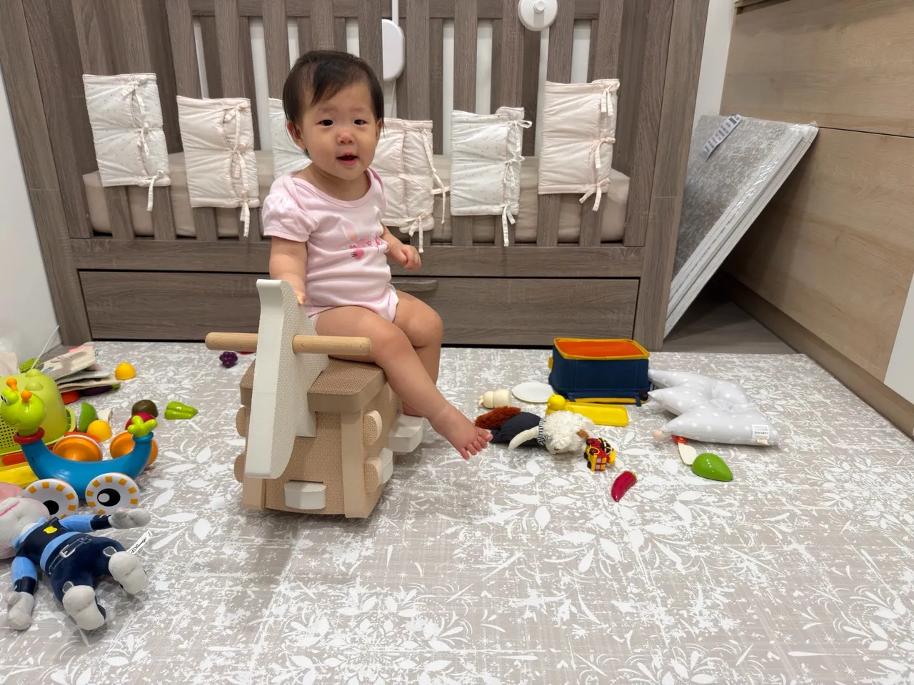 孩子坐在搖搖馬上，床邊鋪著我們家使用的米色枝葉 Playzu 地墊