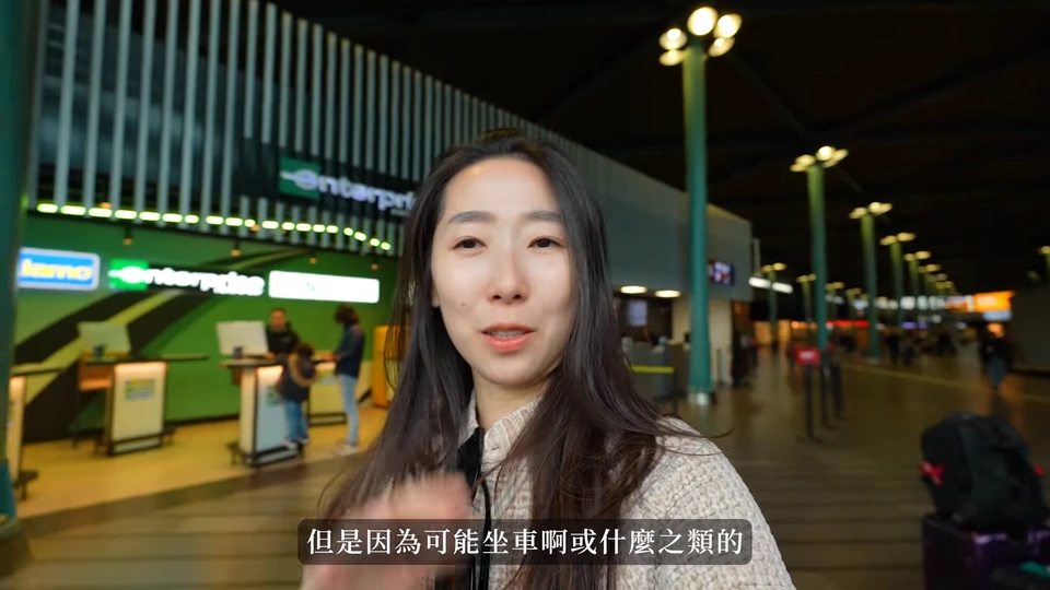 媽媽站在機場租車櫃檯區,後方可見租車品牌