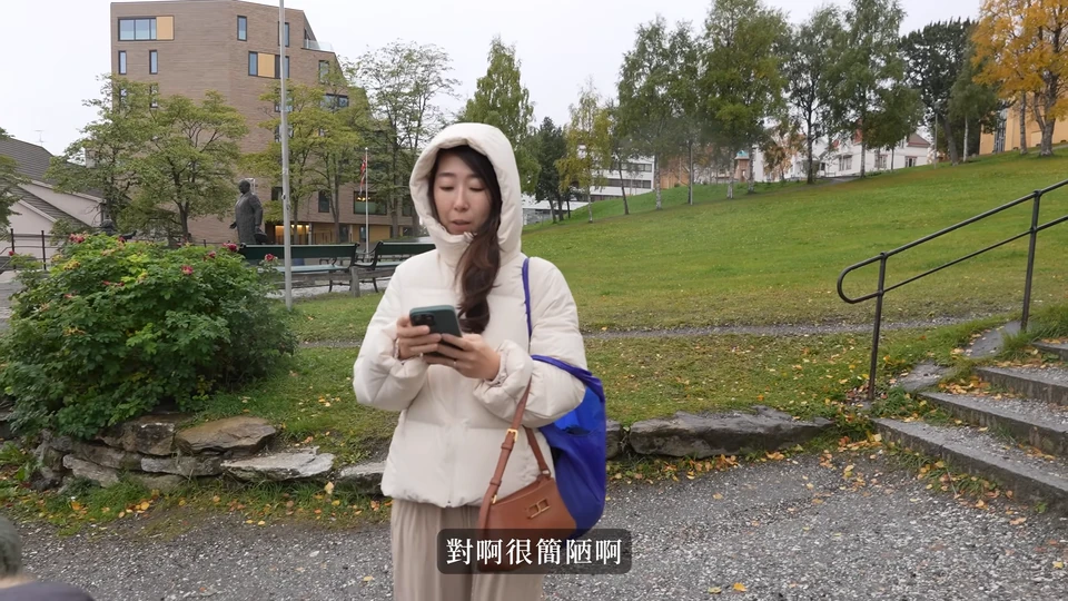 媽媽在街道上看手機,後方是綠色山坡