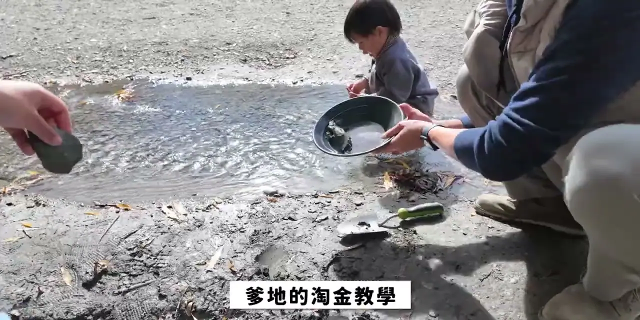 家人在 Arrowtown 河邊手持淘金盤,沿著河灘淘洗砂石