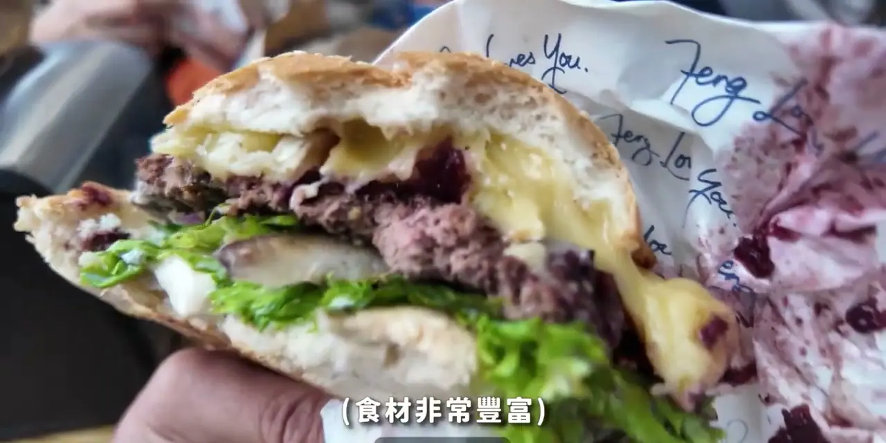 手持剖開的 Fergburger 漢堡,能看到麵包、肉排與蔬菜