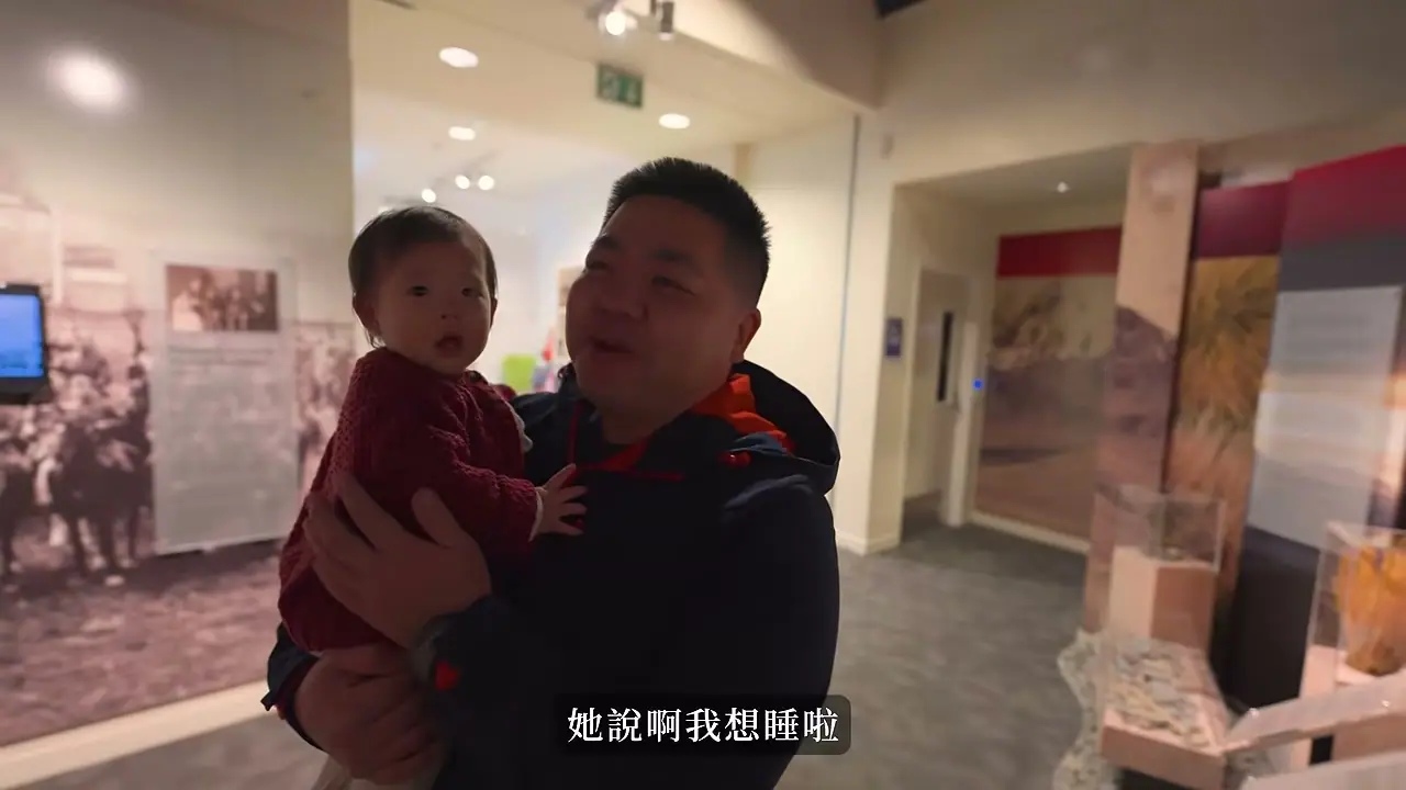 大人抱著幼兒參觀 Ashburton Museum,後方可見地方歷史展板