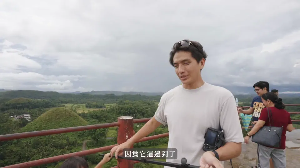 康先生站在巧克力山觀景平台的紅色欄杆旁,後方是丘陵。