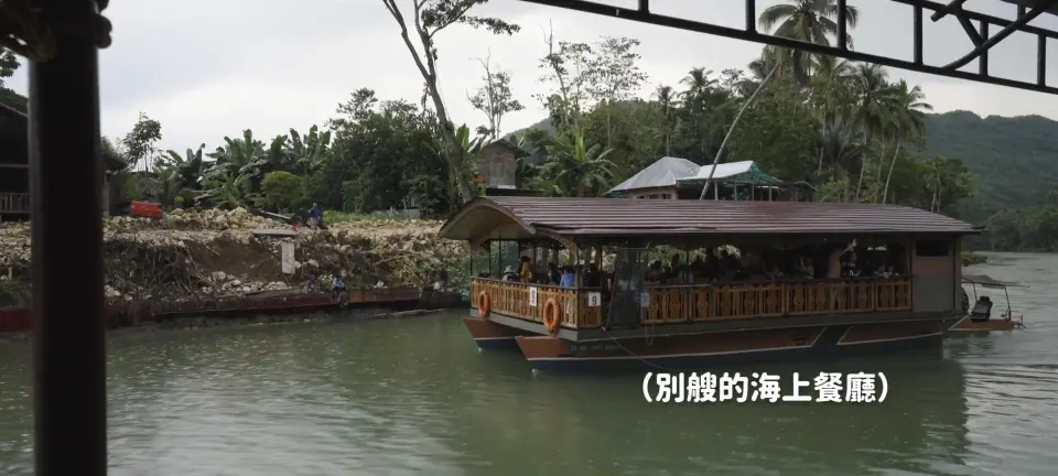 Loboc 河上另一艘有頂篷、座位與乘客的餐飲船,後方是河岸。