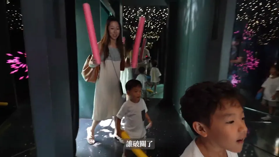 秀秀拿著粉紅色泡棉棒,兩個哥哥站在她前方,鏡子迷宮四周映出多重倒影。