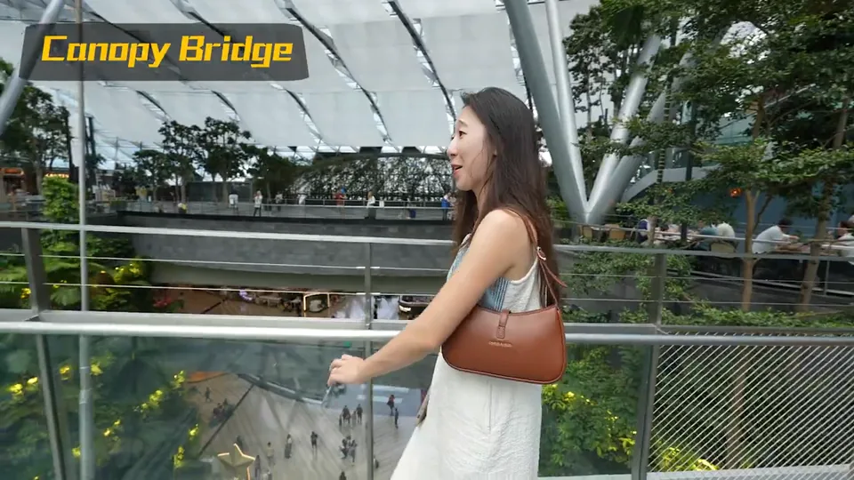 秀秀站在 Canopy Bridge 的玻璃欄杆旁,後方有室內植栽與步道。