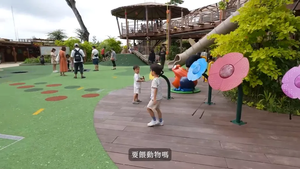 兩個哥哥站在動物園兒童遊戲區,旁邊有滑梯與彩色花朵造型設施。