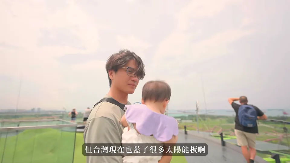 海瑞抱著妹妹站在擎天樹觀景台的欄杆旁,身後可見綠地與遠景。
