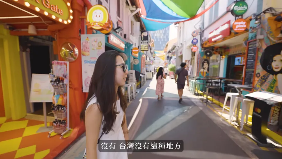 秀秀站在哈芝巷的彩色街屋旁,兩側有店面、招牌與遮陽布。