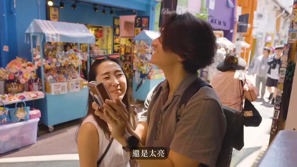 海瑞與秀秀站在藍色紀念品店外交談,海瑞手上拿著手機。