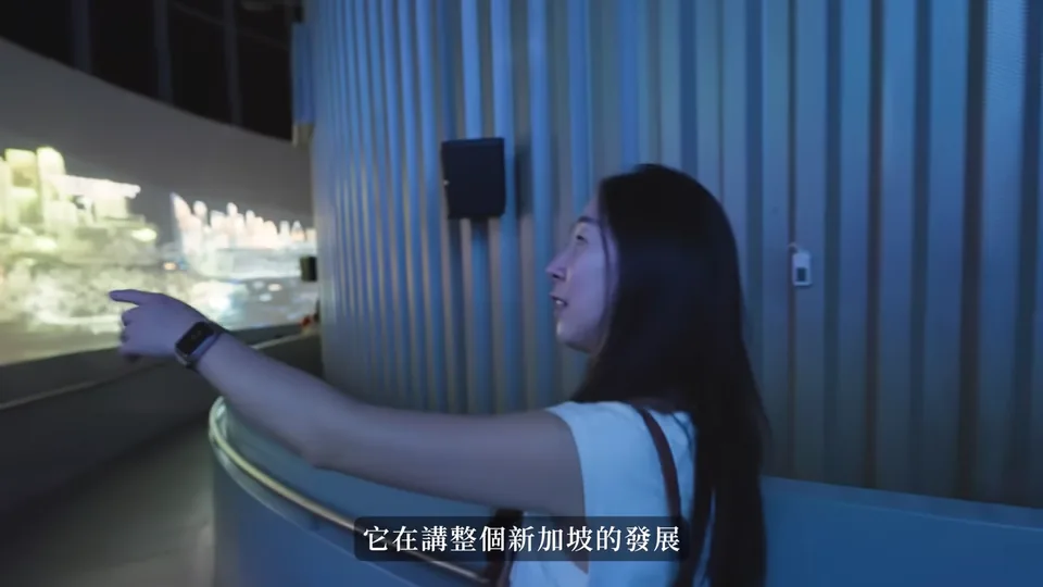 秀秀在 Singapore Odyssea 的藍色光影展區,指向弧形影像展示。