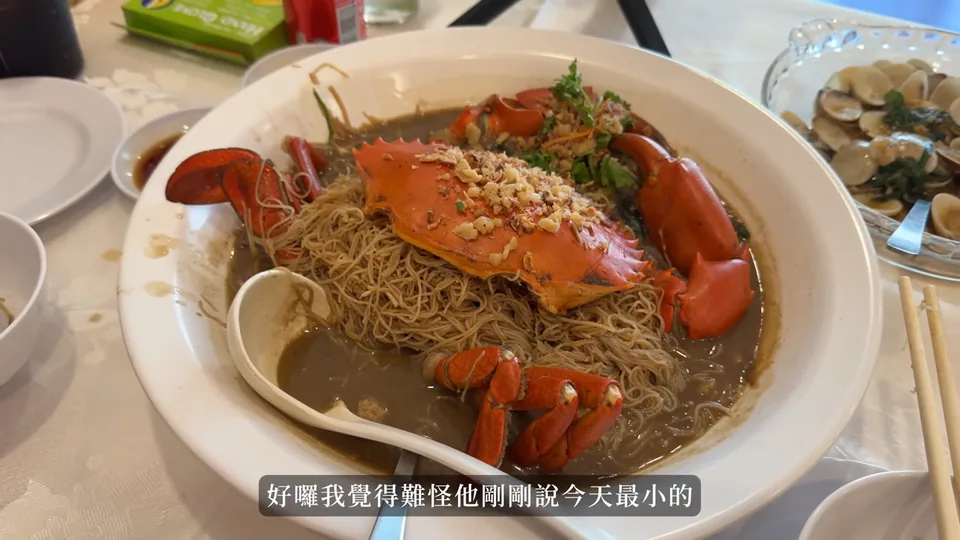 一大盤螃蟹米粉放在餐桌上,紅色蟹殼和蟹螯鋪在米粉與湯汁上,旁邊有其他菜盤
